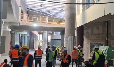 קבוצת עובדים של פילו אש עם אפודים כתומים עוד מספר אנשים עם אפודים ירוקים נמצאים בתוך מבנה באתר בניה. הפרויקט - איטום מעברי אש.